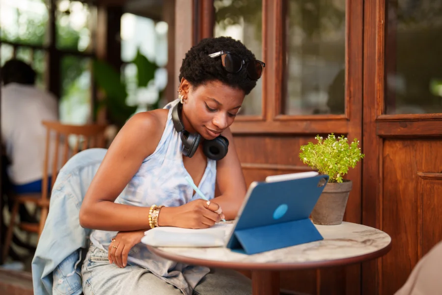 African American female civics education teacher sitting at laptop outside café learning about the ethical use of AI in education.